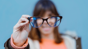 out of focus woman holding up her eye glasses, which are in focus